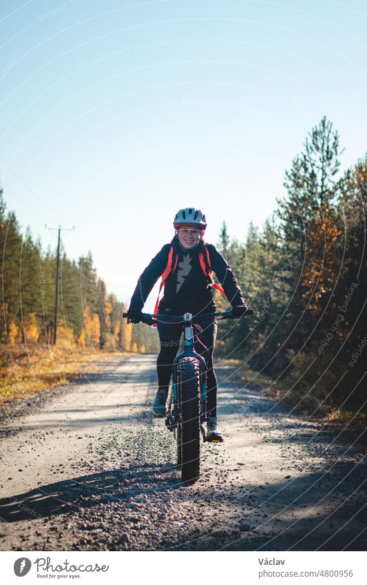 Junge sympathische Frau mit einem schönen realistischen Lächeln beim Freizeitsport. Radfahrer auf einem Fatbike in der wilden finnischen Natur. Gebiet Vuokatti. Radfahrerkleidung und Helm