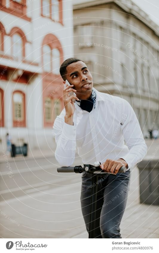 Junger Afroamerikaner, der ein Mobiltelefon benutzt, während er mit einem Elektroroller auf einer Straße steht aktiv Aktivität Afrikanisch Amerikaner attraktiv