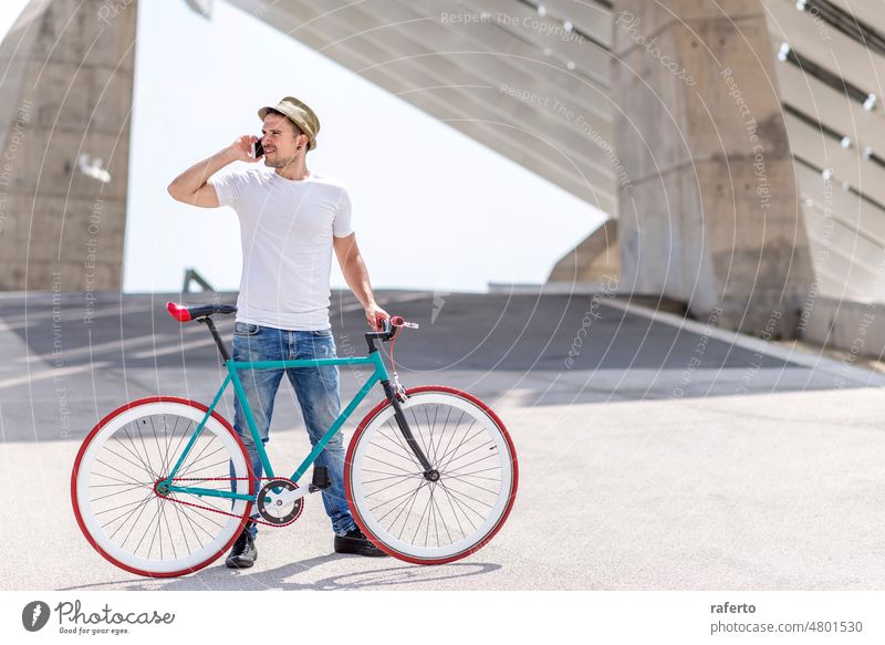 Outdoor-Porträt eines gut aussehenden jungen Mannes mit Mobiltelefon und Fahrrad mit festem Gang auf der Straße. Stehen Beteiligung Telefon Fixie feststehend