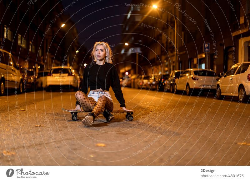 Junge Frau in Shorts auf einem Longboard mit Blick auf die Kamera bei Nacht in der Stadt Vorderansicht sinnlich jung schauende Kamera Wand charmant Mädchen