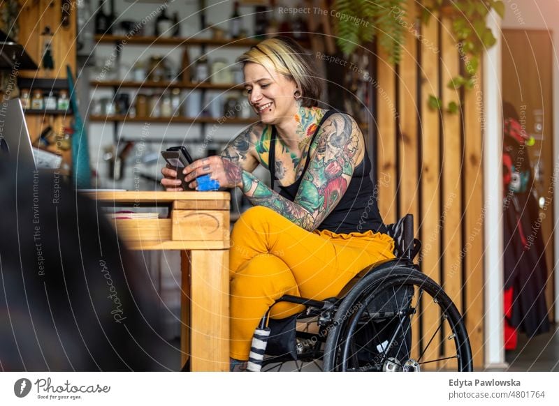 Junge Frau im Rollstuhl benutzt Smartphone zu Hause häusliches Leben Selbstvertrauen im Innenbereich heimwärts Menschen jung Erwachsener lässig Kaukasier
