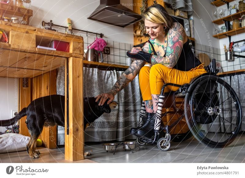 Junge Frau mit Behinderung mit ihrem Hund zu Hause Rollstuhl häusliches Leben Selbstvertrauen im Innenbereich heimwärts Menschen jung Erwachsener lässig