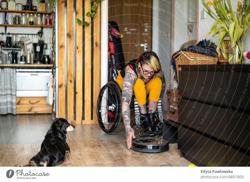 Frau im Rollstuhl justiert intelligenten Reinigungsroboter zu Hause häusliches Leben Selbstvertrauen im Innenbereich heimwärts Menschen jung Erwachsener lässig