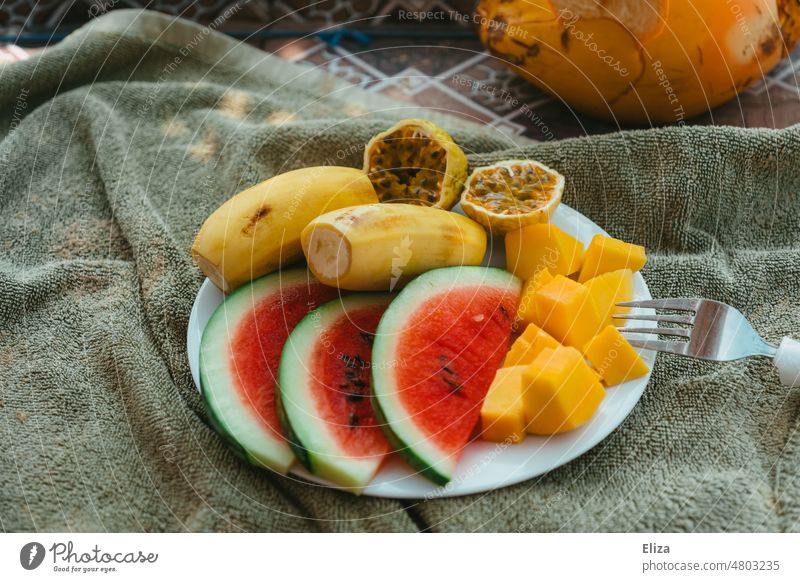 Obstteller mit tropischen Früchten auf Handtuch Wassermelone Maracuja Passionsfrucht Mango Banane gesund Snack Gesunde Ernährung Teller bunt Vitamine Sommer