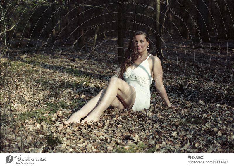 analoges Kleinbild-Portrait einer jungen Frau in weißem Kleid, die in einem Wald sitzt junge Frau schön feminin weiblich Identität authentisch ästhetisch