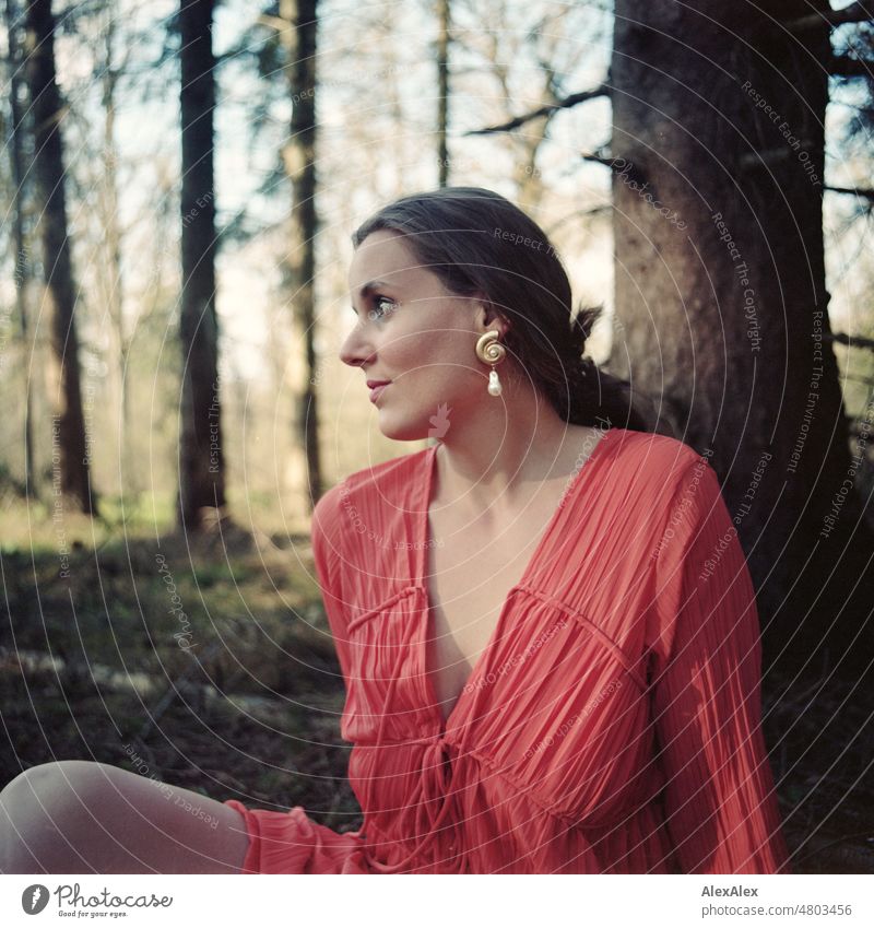 analoges Mittelformat-Portrait einer jungen Frau in orangem Kleid, die in einem Wald sitzt junge Frau schön feminin weiblich Identität authentisch ästhetisch