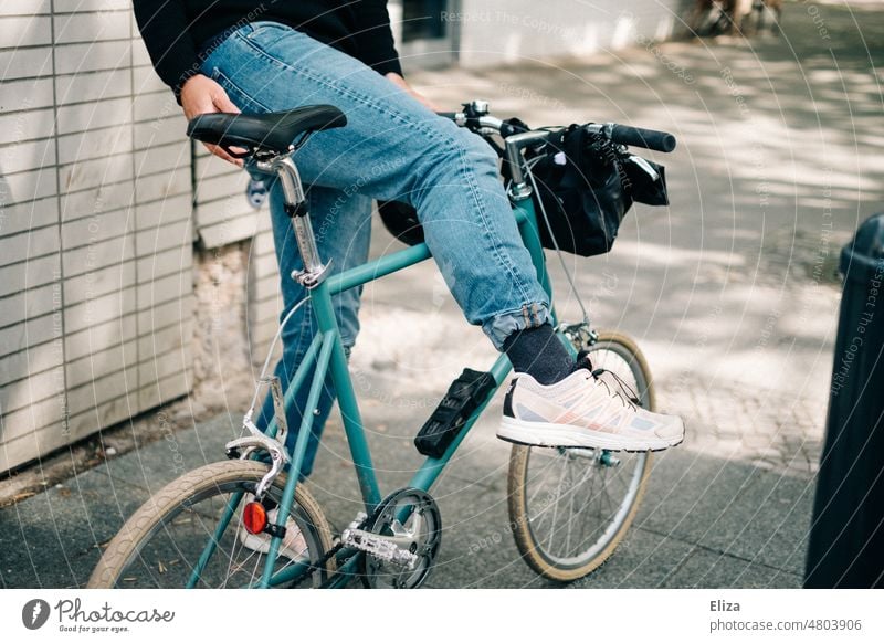 [hansa BER 2022] Mann in Jeans steigt auf sein hippes kleines blaues Stadtfahrrad Fahrrad aufsteigen stadtfahrrad Hipster Sneaker weiß sonnig urban Lifestyle