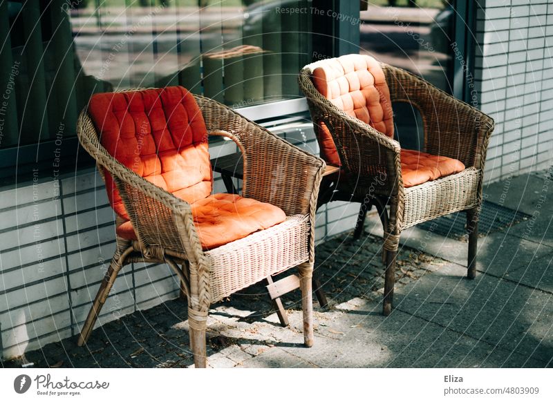 [hansa BER 2022]  Zwei Korbsessel mit roten Sitzkissen genießen die Sonnenstrahlen  vor einem Geschäft zwei leer Sitzplatz Sitzgelegenheit Möbel Sessel orange