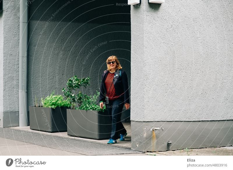 [hansa BER 2022]  Eine Frau mit goldenen  Haaren und Sonnenbrille kommt strahlend lächelnd um die Ecke gelaufen Um die Ecke laufen rot fröhlich Spazieren gehen