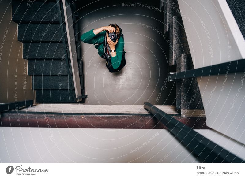 [hansa BER 2022] Eine Frau steht im Treppenhaus und fotografiert mit ihrer Kamera nach oben fotografieren drinnen grün Geländer knipsen Fotografin Gebäude