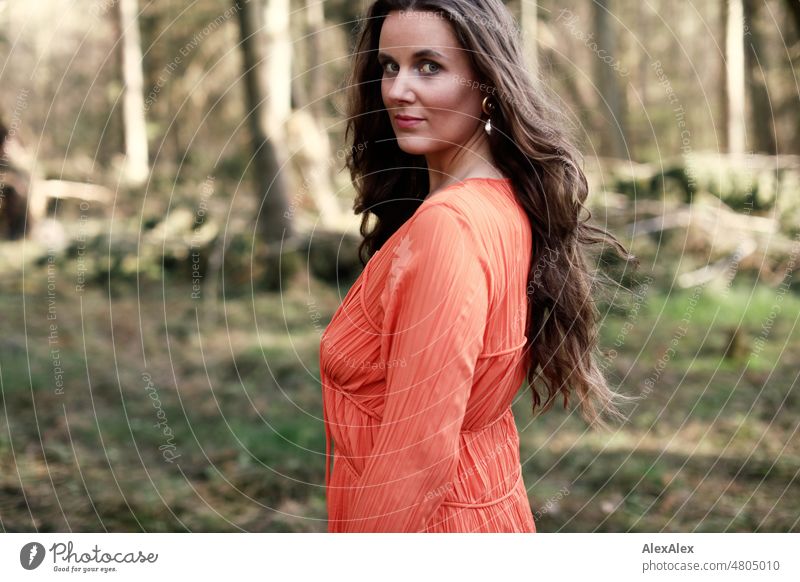 seitliches Portrait einer jungen Frau in orangem Kleid, die in einem Wald steht junge Frau schön feminin weiblich Identität authentisch ästhetisch Erwachsene