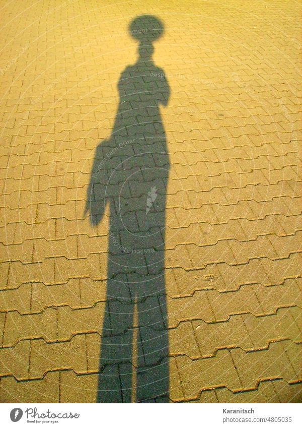 Man sieht die Silhouette einer Lampe und einer Person. Schatten Licht Laterne Straße Morgensonne Selbstportrait