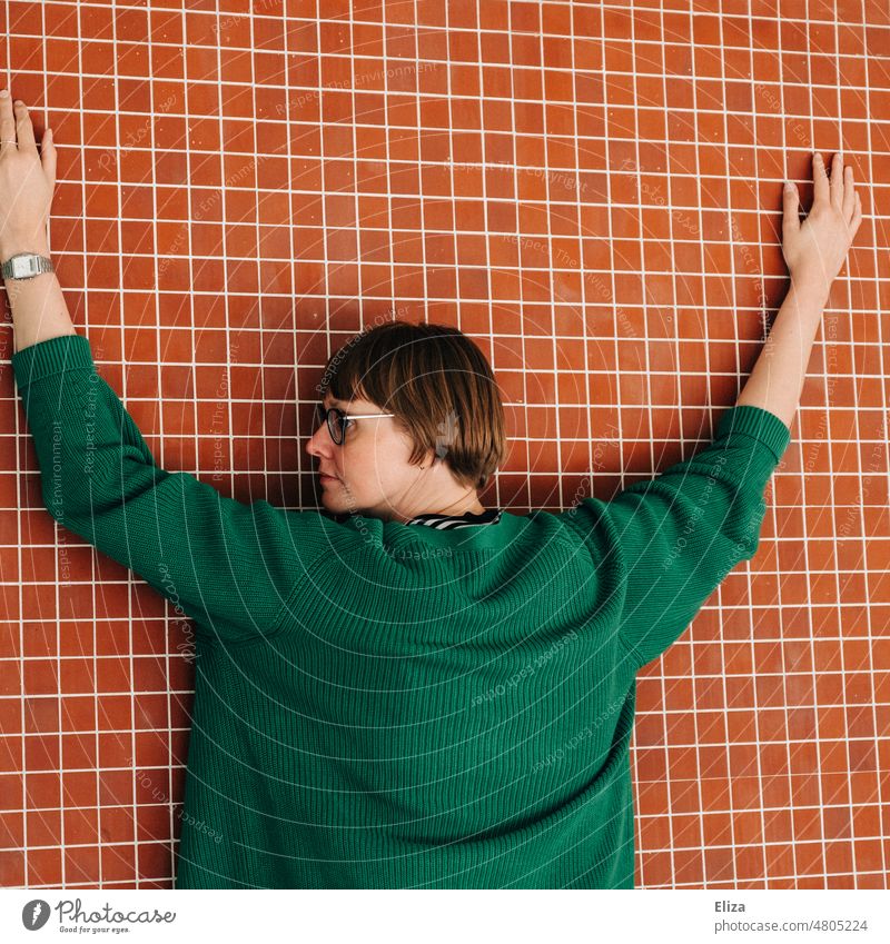 [hansa BER 2022] Frau mit grünem Pulli streckt die Hände an einer rot gekachelten Wand aus ausgestreckt Mensch Arme Kontrast Erwachsene Brille Festnahme Ernst