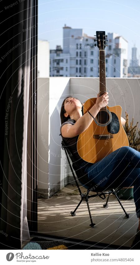 Asiatische Frau mit Gitarre auf Balkon Gitarristen im Freien Sonnenschein asiatisch Hobby Denken Hobbys Freizeit & Hobby Sonnenlicht Sonnenstrahlen