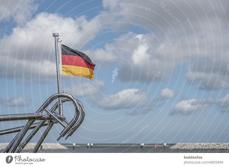 die Edelstahlreling am Heck eines Seglers mit Deutschlandflagge im Hafen mit Sicht auf den Barther Bodden, blauer Himmel mit weißen Wolken Reling