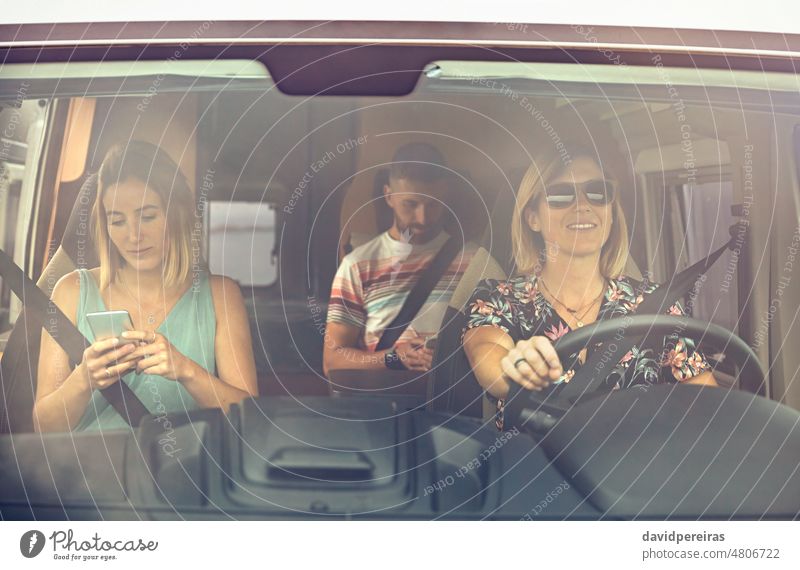 Junge Frau am Steuer eines Wohnmobils und Freunde, die auf ihr Handy schauen Nachricht Mädchen fahren Wohnwagen Kleintransporter Urlaub Ausflug Transport Reise