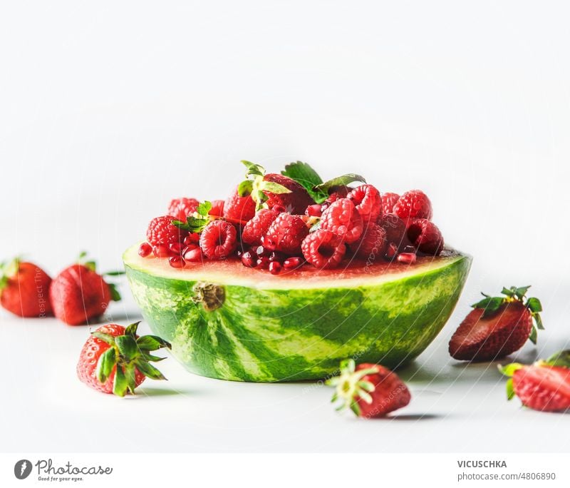 Halbierte Wassermelone gefüllt mit roten Sommerfrüchten auf weißem Hintergrund. halbiert Früchte Himbeeren erdbeeren Granatapfelkerne weißer Hintergrund lecker