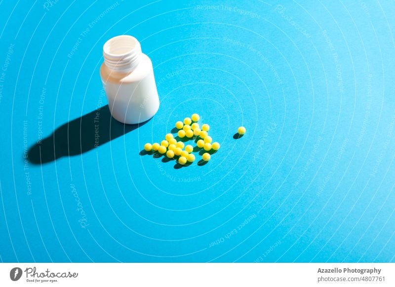 Runde gelbe Kugelpillen und eine Plastikflasche auf blauem Hintergrund. Antibiotikum Ball Flasche Business Kapsel Pflege Chemie Klinik abschließen Konzept