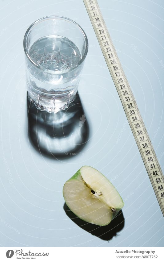 Gesunder Lebensstil Diät Konzept Layout. Glas Wasser mit Apfelscheibe und ein Maßband auf blauem Hintergrund. aqua Getränk Körper Pflege Sauberkeit Kaltwasser