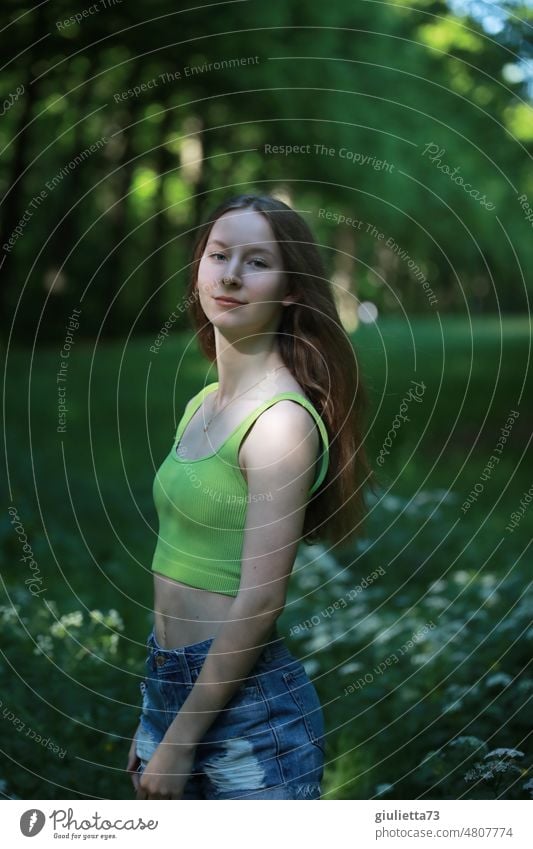 Sommerliches Porträt eines langhaarigen Teenager Mädchens mit kurzen Jeansshorts und bauchfreiem Top im Park Mensch Junge Frau Mai Juni Jugendliche Farbfoto