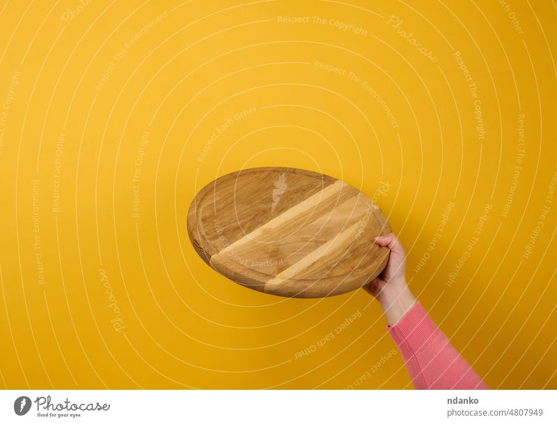 Frau hält leeres rundes Holzpizzabrett in der Hand, Körperteil auf gelbem Hintergrund Holzplatte braun Kaukasier Küchenchef hacken kreisen Koch Schneidebrett