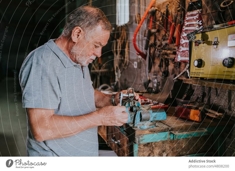 Ein älterer Mann befestigt ein Metallteil mit Ratsche und Schraubstock Reparatur Detailaufnahme fixieren Hobelbank Werkstatt schäbig männlich Senior Fokus