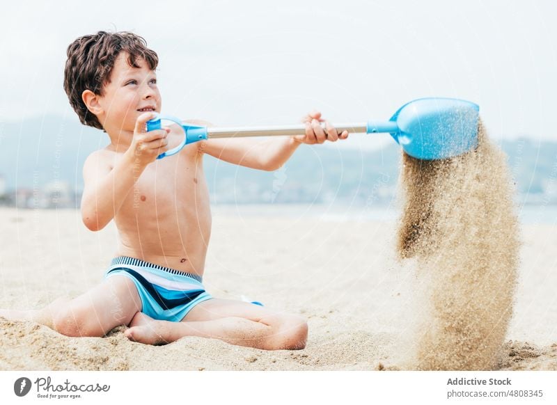 Fröhlicher kleiner Junge gräbt Sand am Strand Graben Sommer Urlaub Lächeln schaufeln Wochenende froh Kind Küste sich[Akk] entspannen Ufer knien Kindheit ruhen