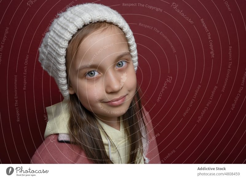 Fröhliches Mädchen mit warmer Mütze und Blick in die Kamera im Studio Kind Hut gestrickt Stil Porträt trendy Outfit lange Haare Oberbekleidung warme Kleidung