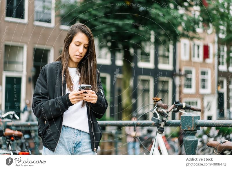 Fokussierte junge hispanische Frau, die auf einer Brücke über einen Kanal ihr Smartphone benutzt Nachricht Reisender Urlaub Großstadt benutzend Ausflug Mobile
