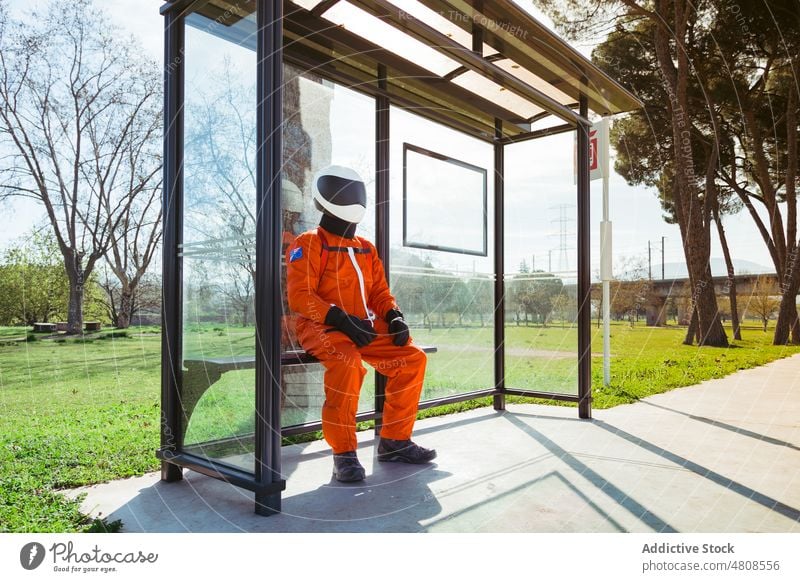 Unbekannter Kosmonaut in orangefarbenem Anzug sitzt an der Bushaltestelle Astronaut warten Raumanzug Öffentlich futuristisch Station Bank Raumfahrer