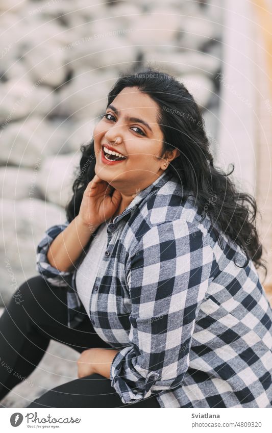 Straßenporträt eines indischen Mädchens in einem karierten Hemd im Freien jung Porträt schön Inder Sitzen Lächeln sitzen Streetstyle asiatisch Frau Mode trendy