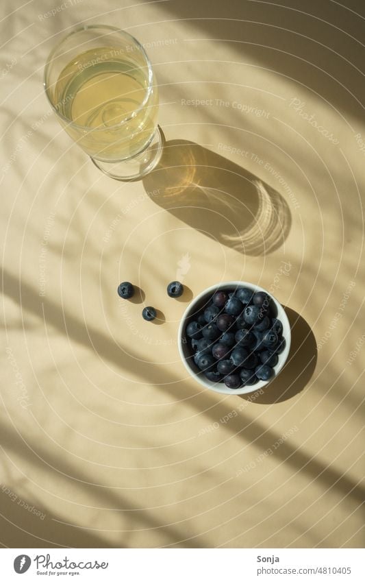 Ein Glas Wein und frische Blaubeeren auf einem beigen Tisch. Schlagschatten. weiß Sonnenlicht Silhouette Schatten Schattenspiel Strukturen & Formen Licht