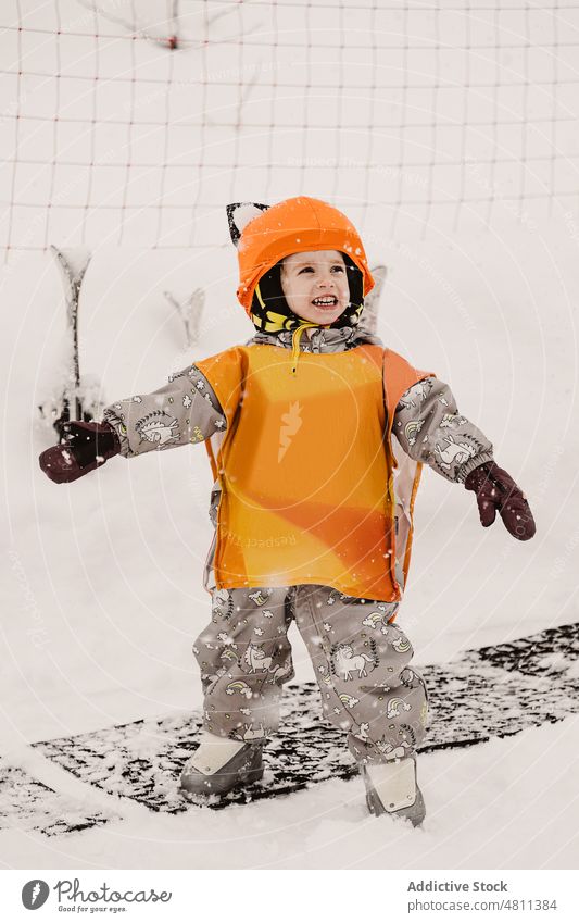Fröhliches Kind in Winteroverall und Helm lächelnd in verschneitem Terrain Lächeln Schnee Skifahrer Skigebiet Aktivität heiter gesamt Kindheit Feiertag Hobby