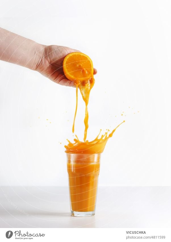 Frauen Hand Auspressen von Orangen mit Spritzen Saft in Glas auf weißem Hintergrund. quetschend orange Geplätscher weißer Hintergrund Orangensaft Vorbereitung
