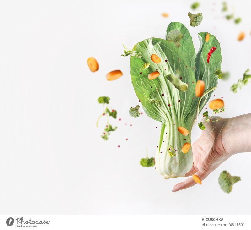 Frauenhand, die rohen Bok Choy und fliegendes Gemüse auf weißem Hintergrund hält. Hand Beteiligung Bok Choi weißer Hintergrund gesunde Ernährung Diätnahrung