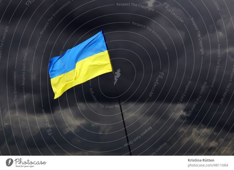 ukraine fahne vor dunklen wolken flagge nationalfarben bedrohlich bedroht symbolisch symbolbild wehen flattern himmel dunkel bewölkt blau gelb erde solidarität