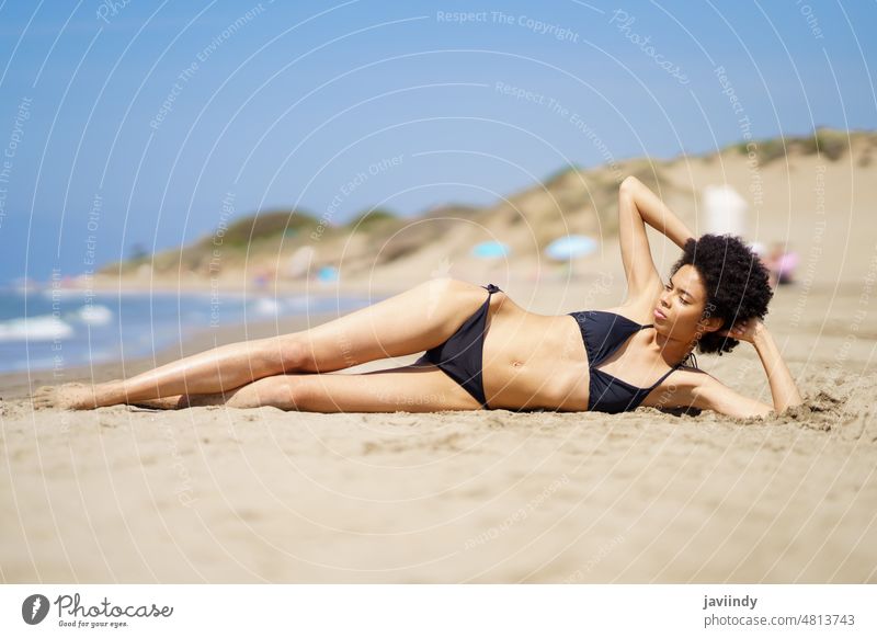 Entspannte schwarze Frau, die auf dem Sand eines tropischen Strandes liegt und ein Sonnenbad nimmt. Bikini Sommer Badeanzug Afro-Look Frisur