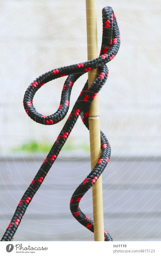 schwarz rotes Absperrseil windet sich eigenwillig um Bambusstab senkrecht Meterware Schlingen Drehungungen Seil Gummi Schnur Band