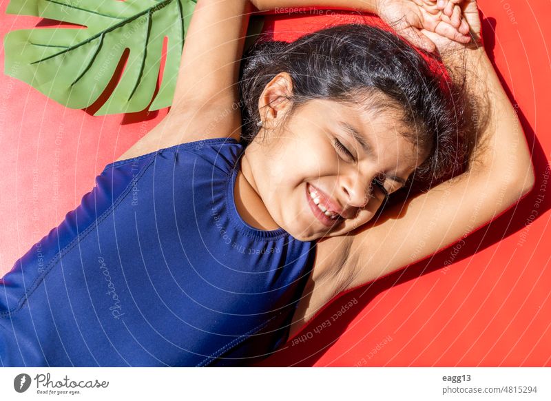 Kleines Mädchen mit Badeanzug empfängt die Sonne mit direktem Licht. Kind Porträt Sonnenbad Limonade trinken Gesichtsausdruck Badebekleidung Pool liegend