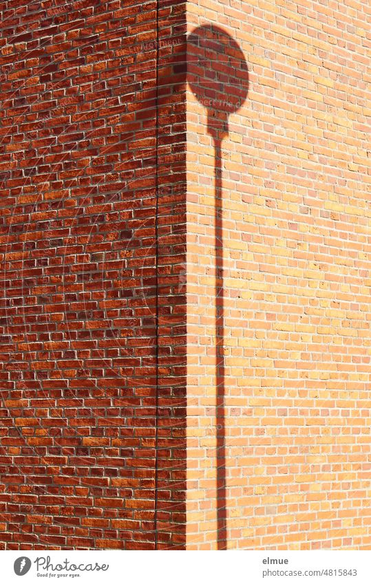 Schatten eines runden Verkehrszeichens mit Stange an der Ecke eines Gebäudes aus roten Ziegeln, das zur Hälfte im Schatten liegt / Minimalismus Schattenspiel