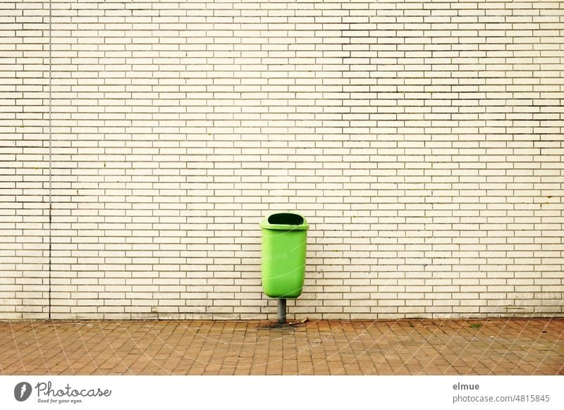grüner Abfallbehälter für Restmüll vor einem Gebäude in beigefarbener Klinkerverkleidung / Müllentsorgung Außenabfallsammler Müllschlucker Papierkorb Stadtleben