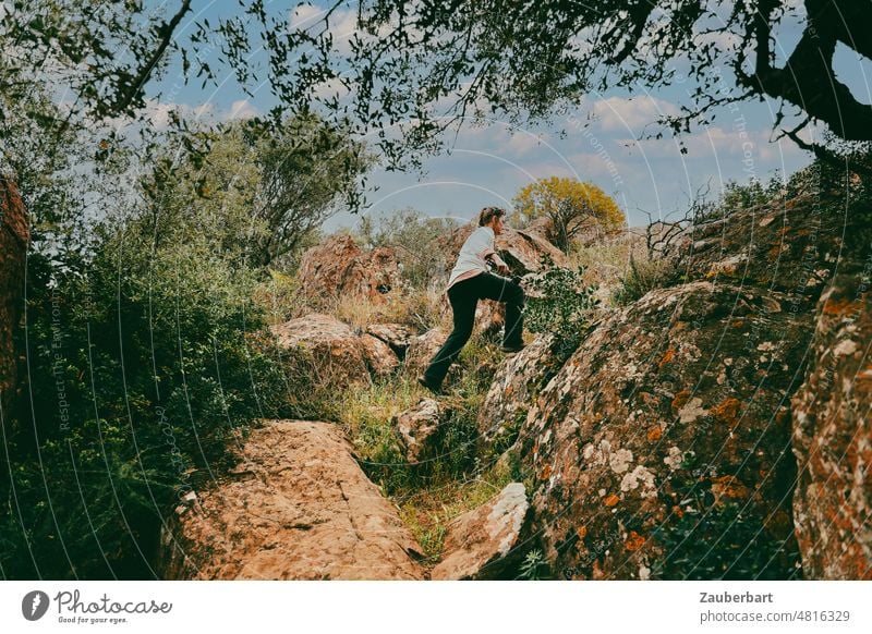 Frau in schwarzer Wanderhose steigt auf einem felsigen Wanderpfad auf Sardinien Pfad Wanderweg wandern steigen aufsteigen Aufstieg Fels Bäume Büsche Landschaft