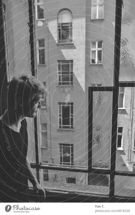 ein junger Mann schaut aus dem Treppenhausfenster nachdenklich in den Innenhof eines alten Berliner Hinterhofes Fenster Prenzlauer Berg s/w blond Stadtzentrum