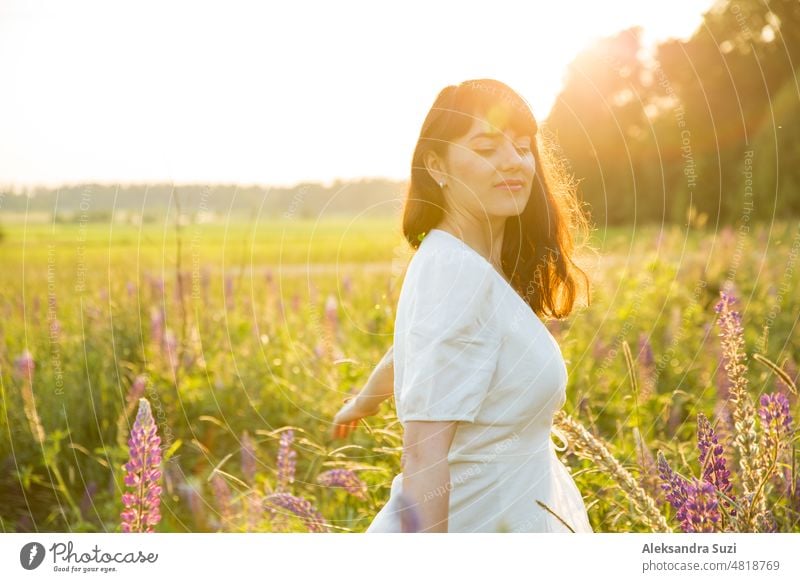 Schöne Frau im weißen Sommerkleid genießt die sommerliche Natur. Pflücken bunte Blumen, atmen frische Luft und Blumenduft, zu Fuß in der sonnigen Feld von Lupinen. Glück Konzept