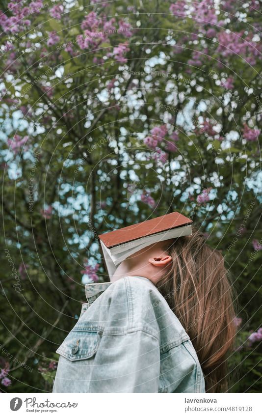 Gesichtslose Aufnahme einer Frau, die sich im Freien ein Buch vor das Gesicht hält Menschen Mädchen Person allein Jeansstoff Bildung gesichtslos grün Hände