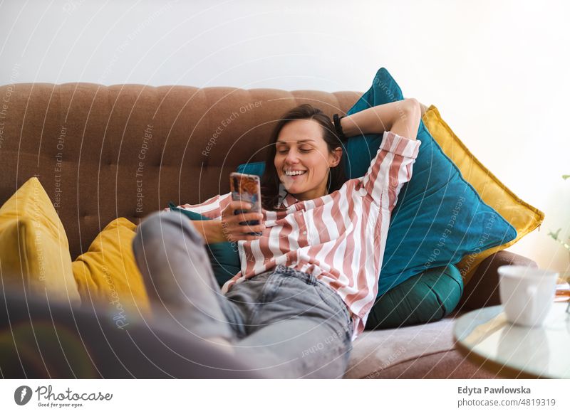 Glückliche junge Frau, die auf dem Sofa ein Mobiltelefon benutzt Handy Smartphone Technik & Technologie online Internet per Telefon Mitteilung häusliches Leben