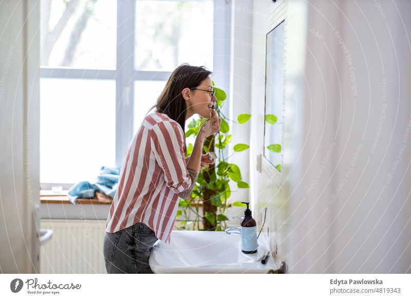 Frau trägt vor dem Badezimmerspiegel Lipgloss auf häusliches Leben Selbstvertrauen im Innenbereich heimwärts Haus Menschen jung Erwachsener lässig Kaukasier
