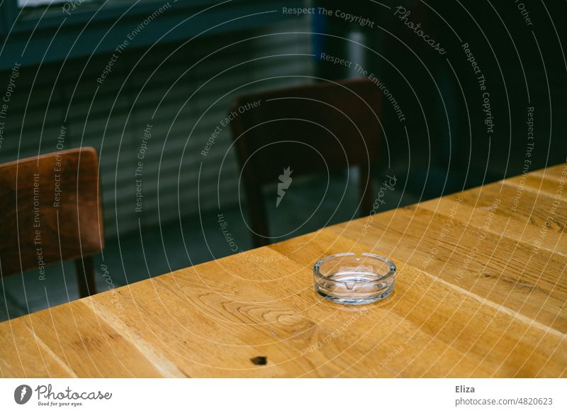 [hansa BER 2022] Leerer Aschenbecher aus Glas auf einem Holztisch Tisch Gastronomie Rauchen Diagonale leer Stühle zwei Menschenleer Café Restaurant Straßencafé