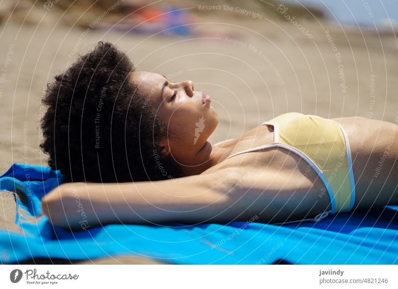 Entspannte schwarze Frau, die auf dem Sand eines tropischen Strandes liegt und ein Sonnenbad nimmt. Bikini Sommer Badeanzug Bräunen Afro-Look Frisur
