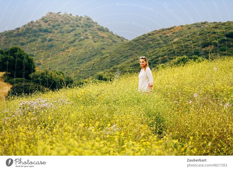 Frau im weißen Pullover steht auf einem Feldweg im gelben Blumenmeer vor einer Hügelkette Ginster schauen Wandern Landschaft Natur Himmel Vegetation Frühling